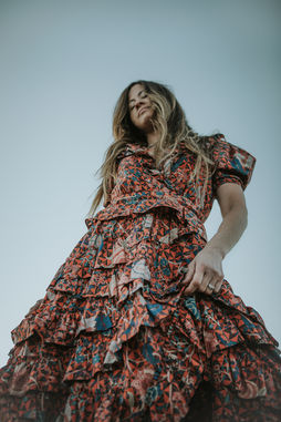 Woman in bohemian dress twirls joyfully with flowing hair against sky