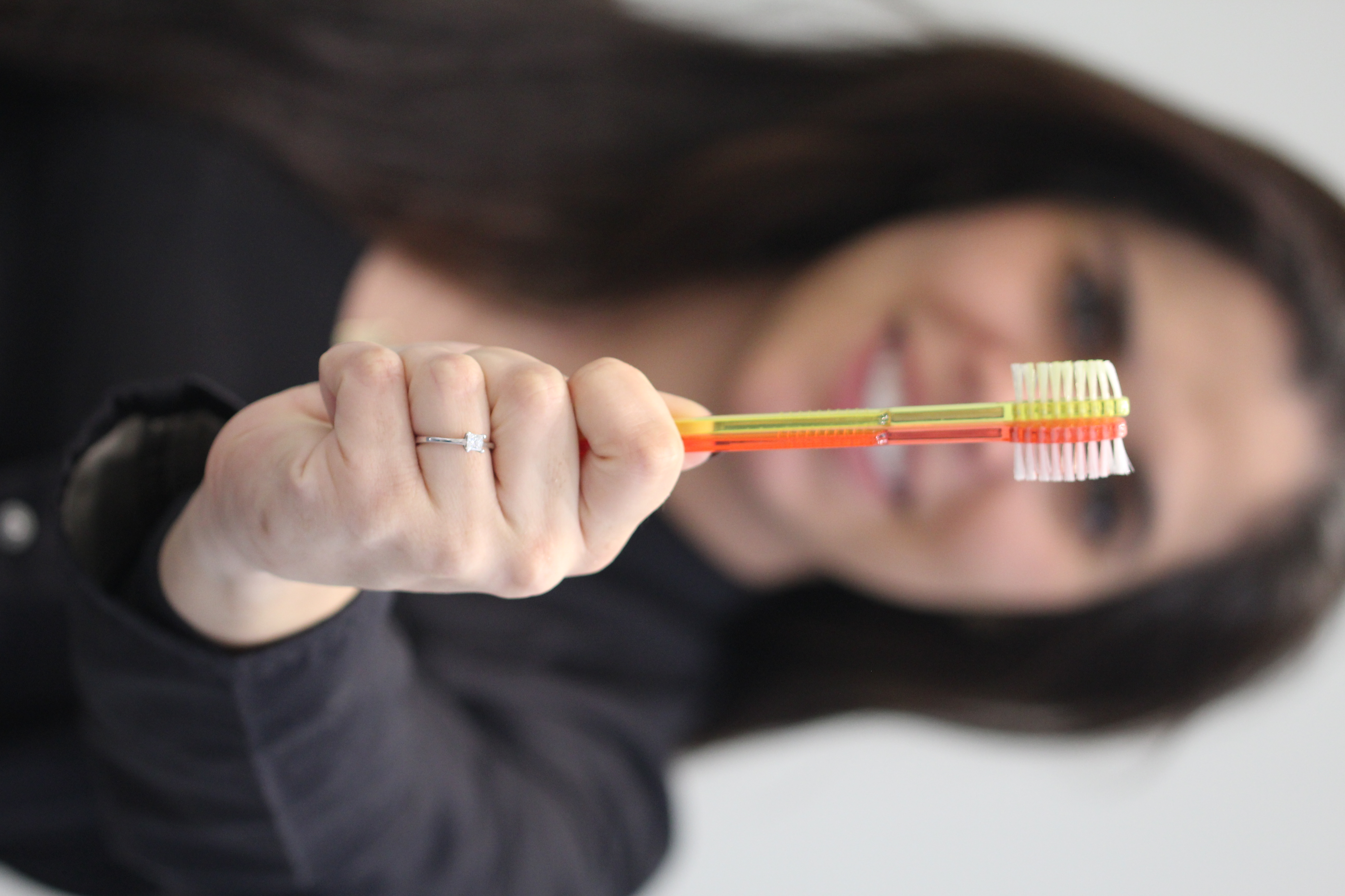 Dr Tatiana Pires en fond flouté tenant 2 brosses à dents en premier plan