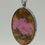 Thumbnail: Close-up of oval resin necklace featuring pink pressed flower and green leaves in silver-tone frame