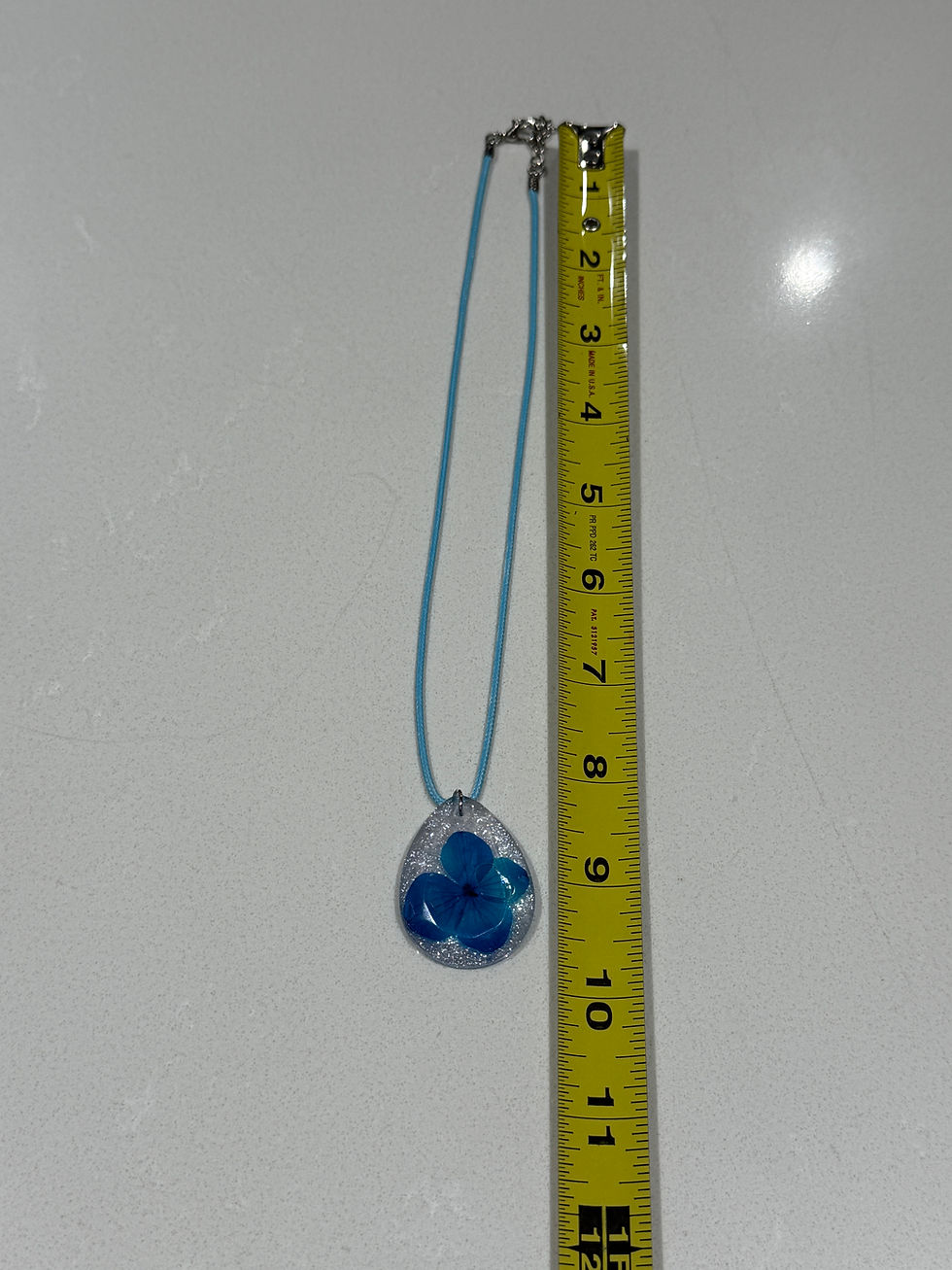 Thumbnail: Blue pressed flower resin necklace with measuring tape showing length