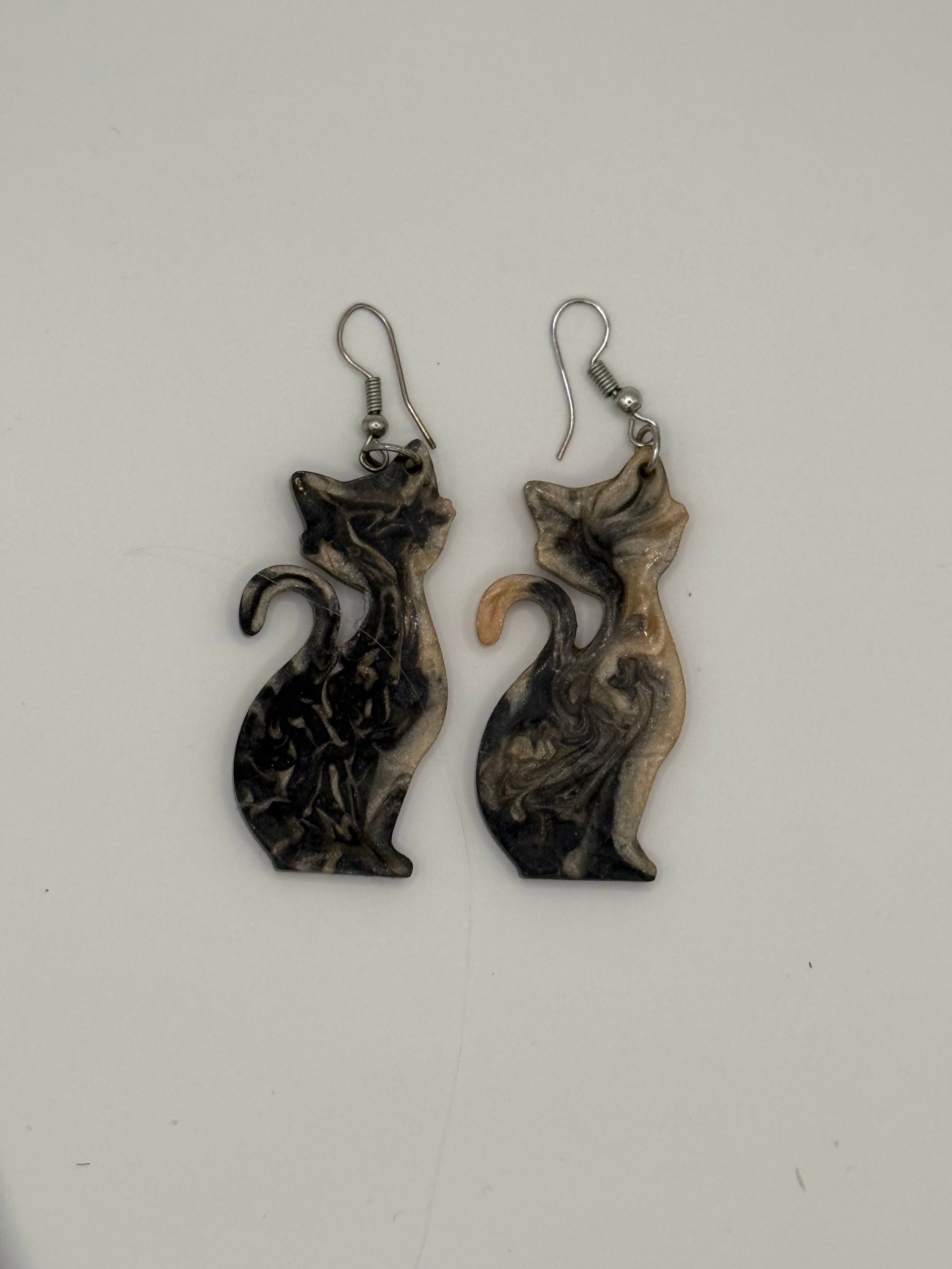 Angled view of handmade resin cat earrings highlighting marbled pattern and curved tail design