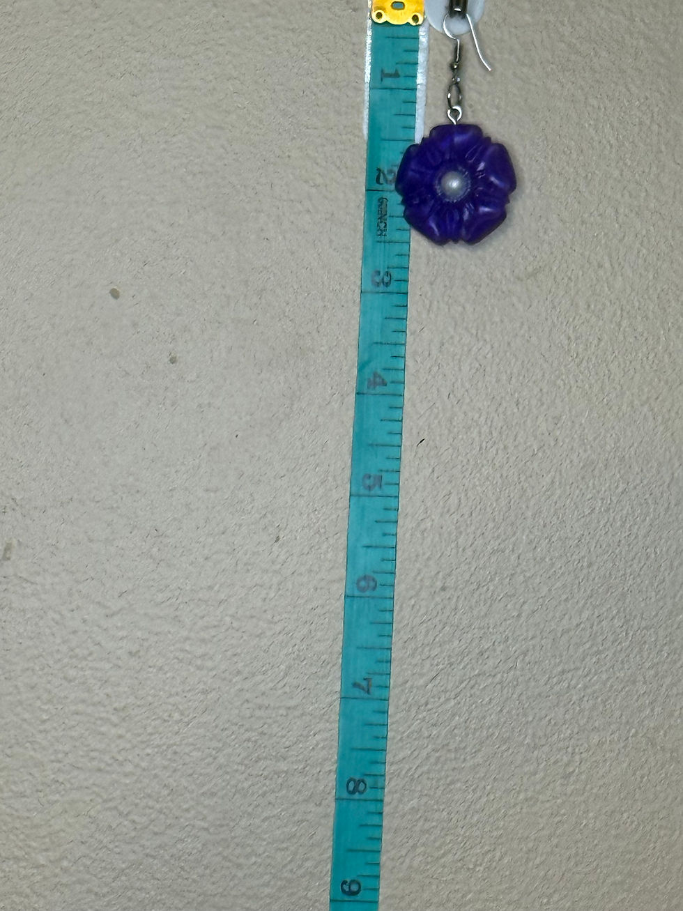 Thumbnail: Purple flower resin earring hanging beside measuring tape to show size and drop length.