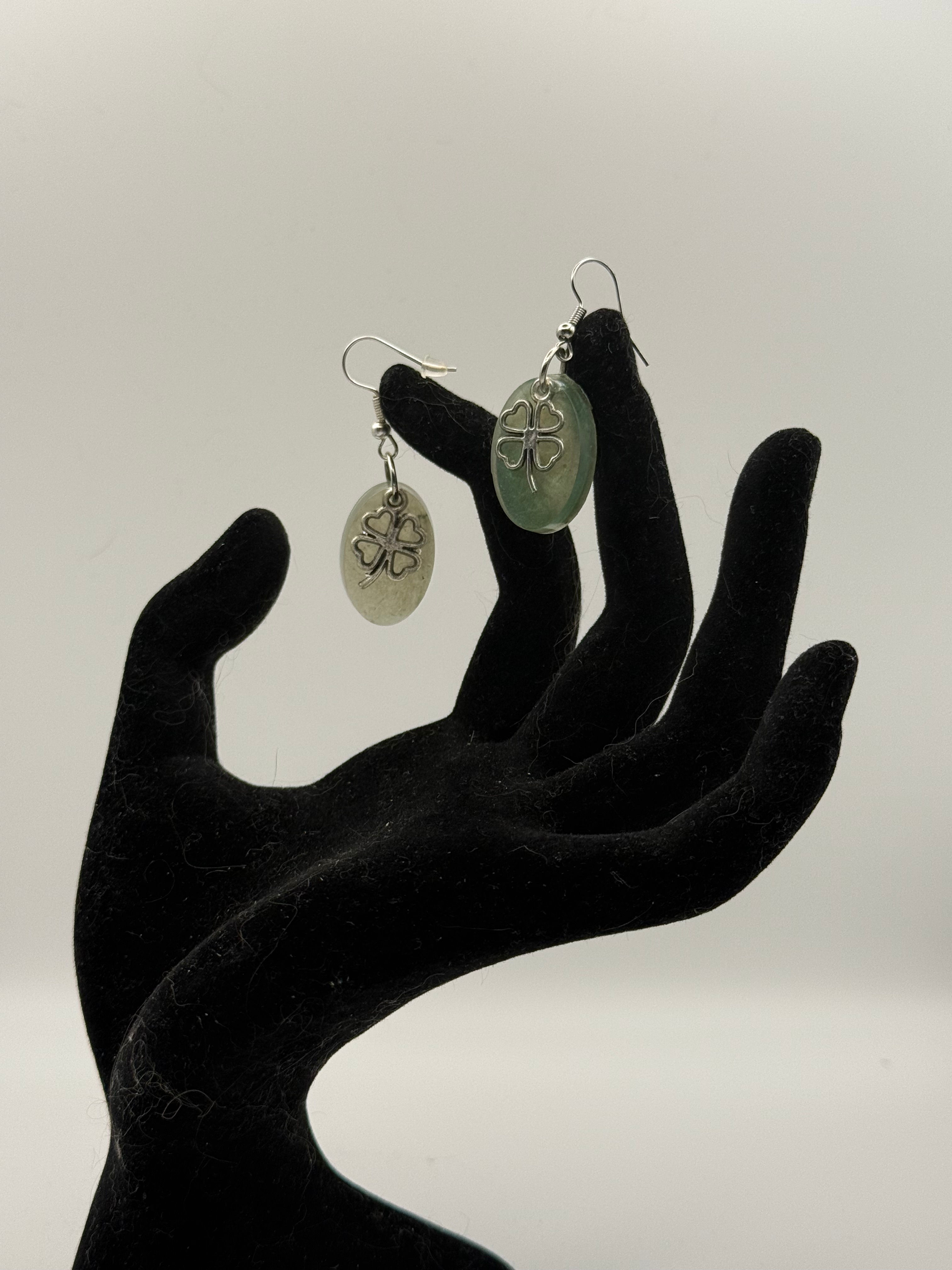 Milky green oval resin earrings with silver four-leaf clover charm on black hand stand, silver fish hook wires