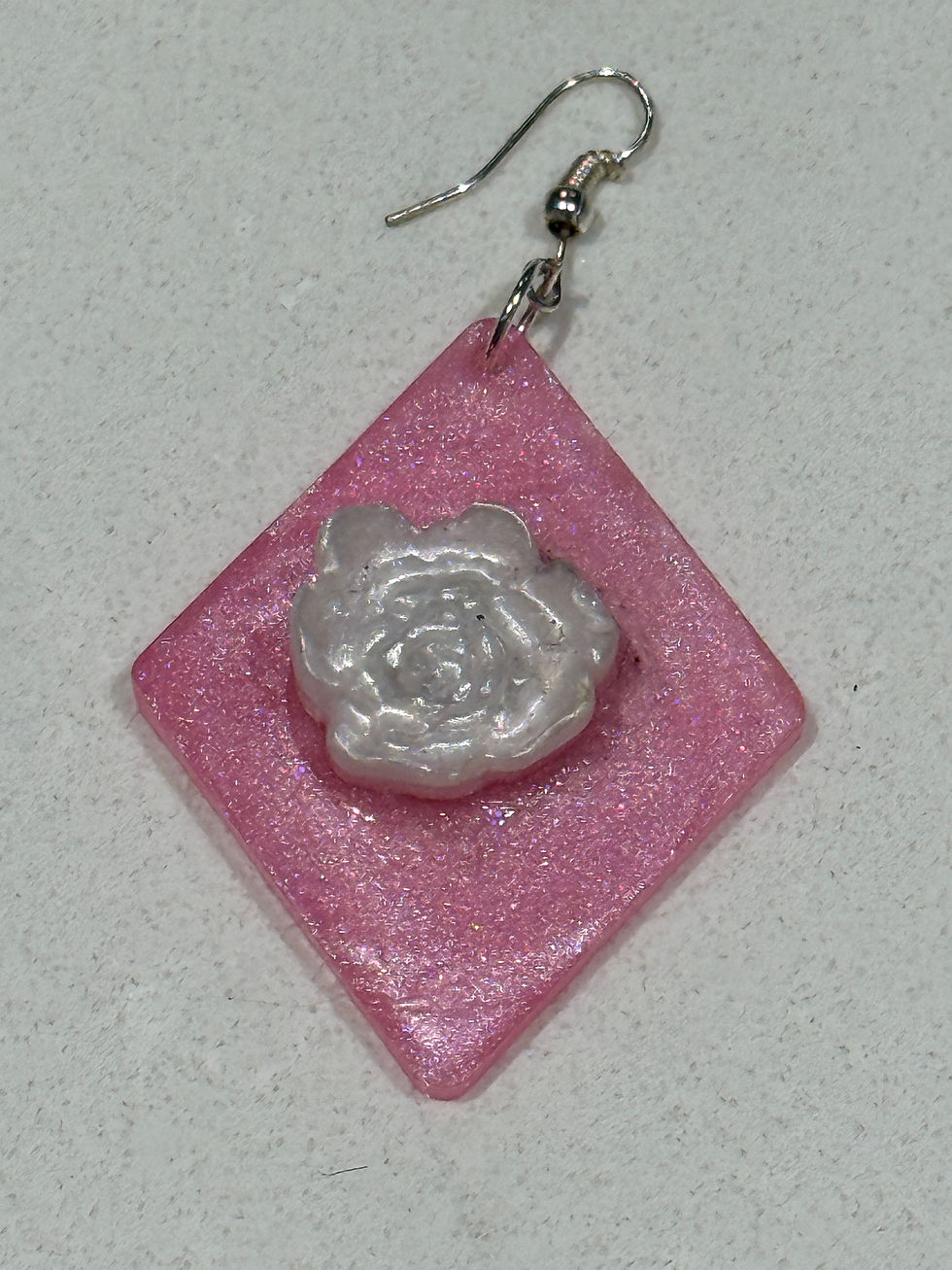Close-up of pink resin earring with raised white rose and sparkle finish