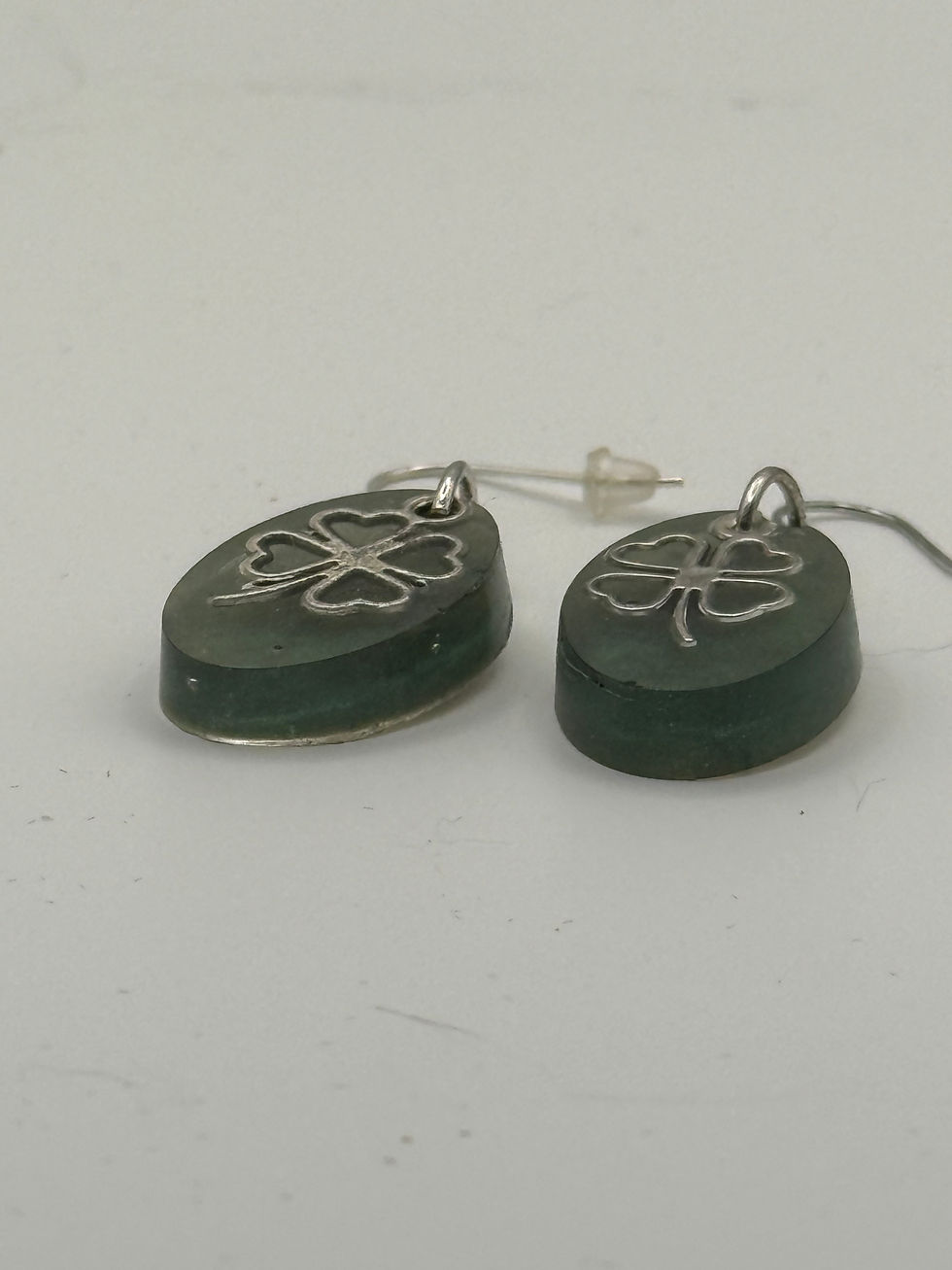 Thumbnail: Both milky green oval resin earrings flat on white surface showing translucent resin depth and silver clover charm