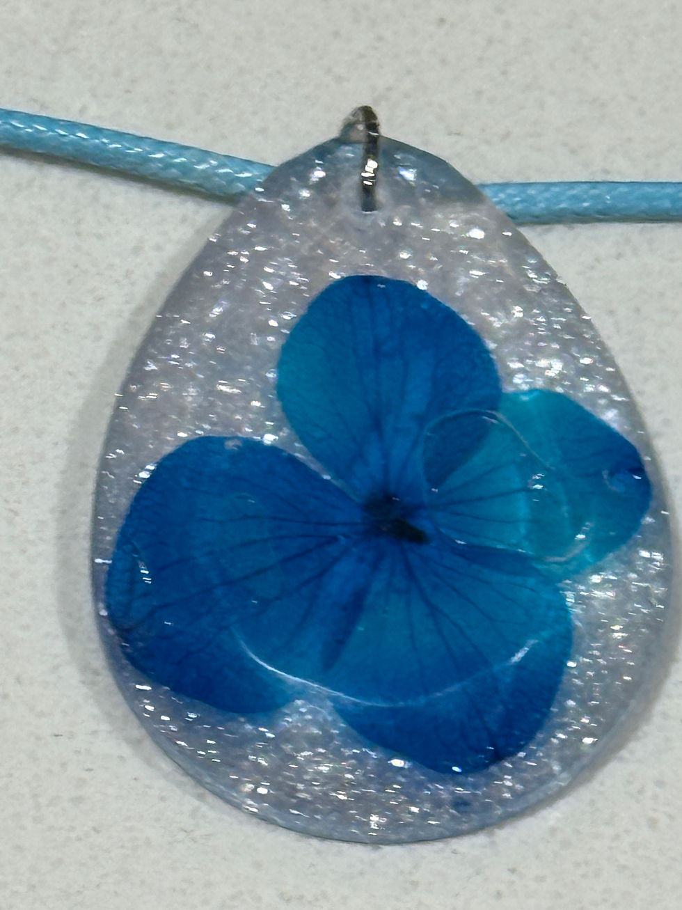 Close-up of blue real flower preserved in clear resin teardrop pendant
