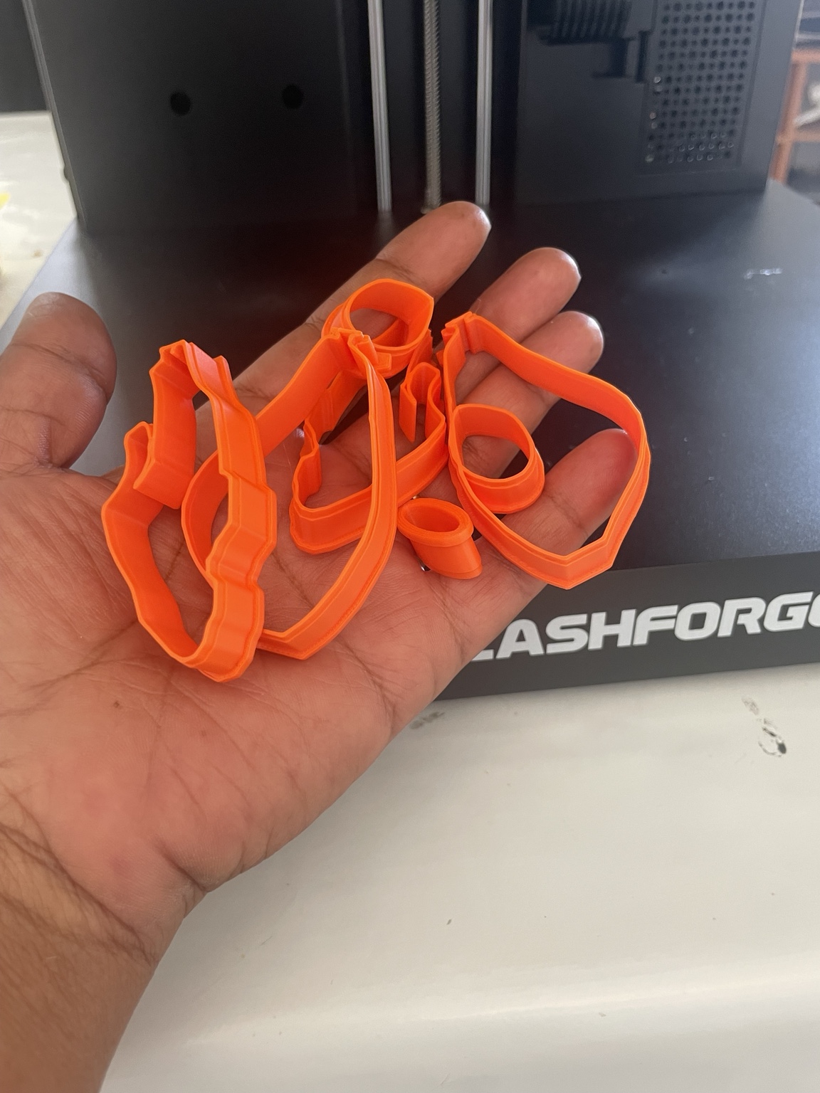 Emporte-pièces orange présentés à la main devant l’imprimante 3D de l’atelier Forméa