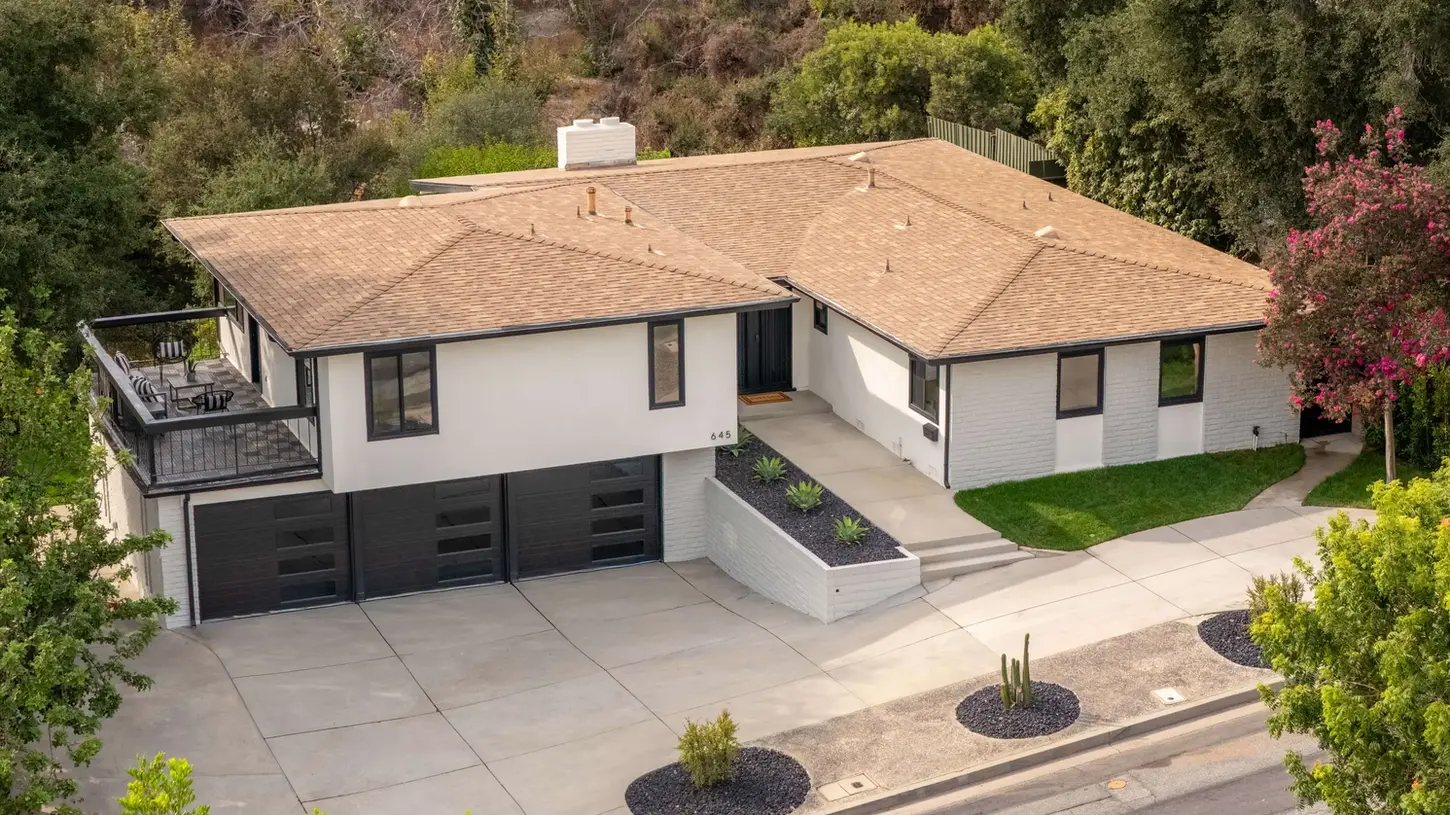 Aerial view of a modern hillside home with a large deck and three-car garage.