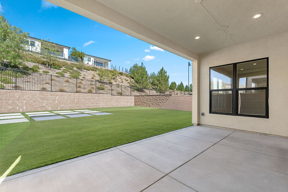 Backyard patio and lawn beside the two-story residence with block retaining wall and hillside landscaping