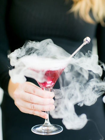 Woman holding a cocktail glass filled with a pink drink and surrounded by dramatic smoke or vapor.