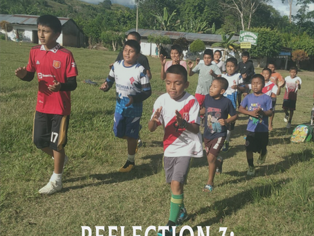 Kids in colorful jerseys run on a grassy field under a blue sky. Text: Reflection 3: A Community That Heals. Background: houses and trees.