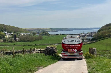 Red fuel tanker driving along a rural road next to a lake
