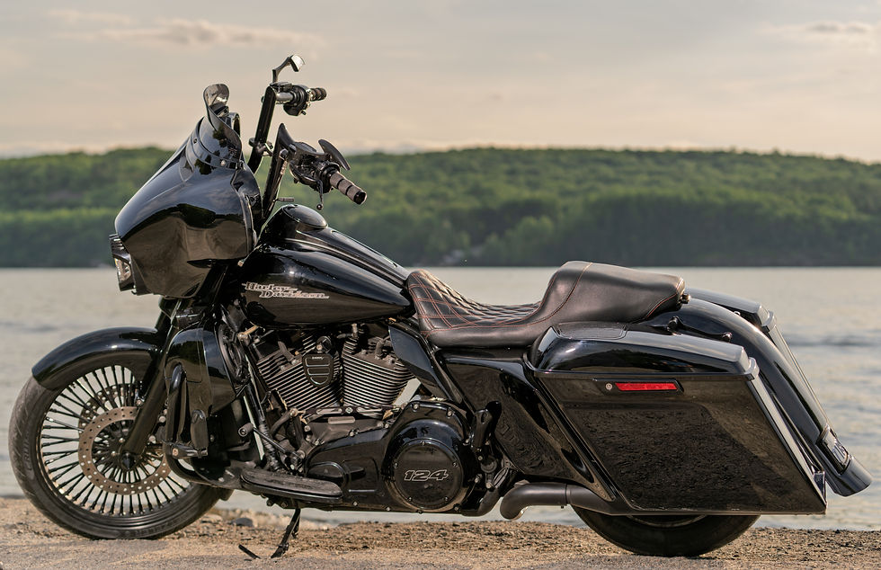 A black Harley-Davidson motorcycle beside a lake at golden hour.