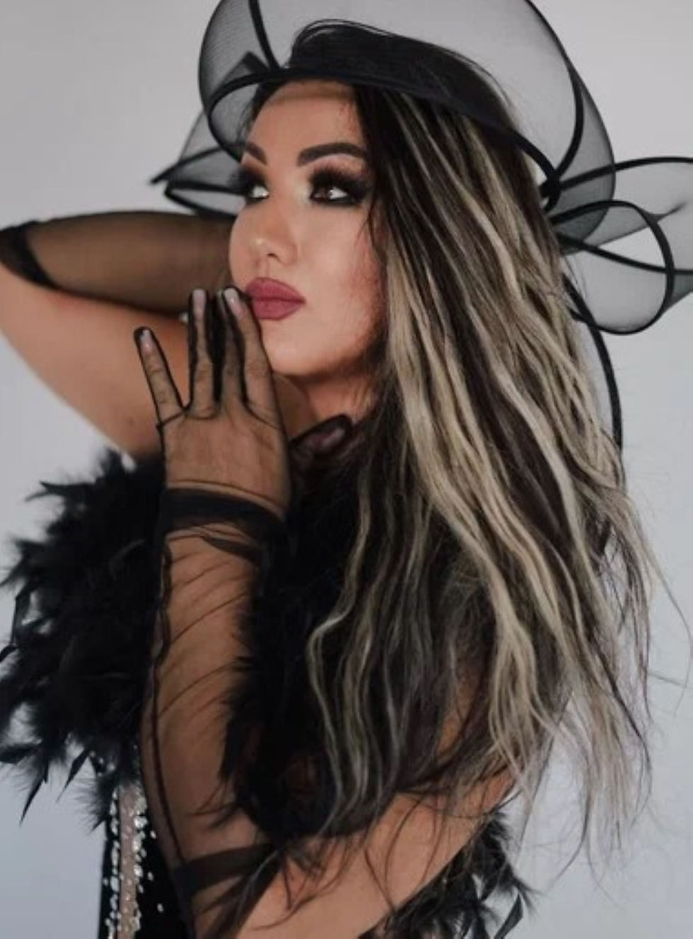 Model Венера Алиева stars in Beautiful Venus, a glamorous studio fashion series featuring dramatic black looks against a minimalist white backdrop. In one portrait, she poses in a voluminous black tulle mini ensemble with sheer sleeves and platform heels; in another, she wears a crystal-embellished black gown with feather detailing and sheer gloves, playfully framing her face with translucent fabric.