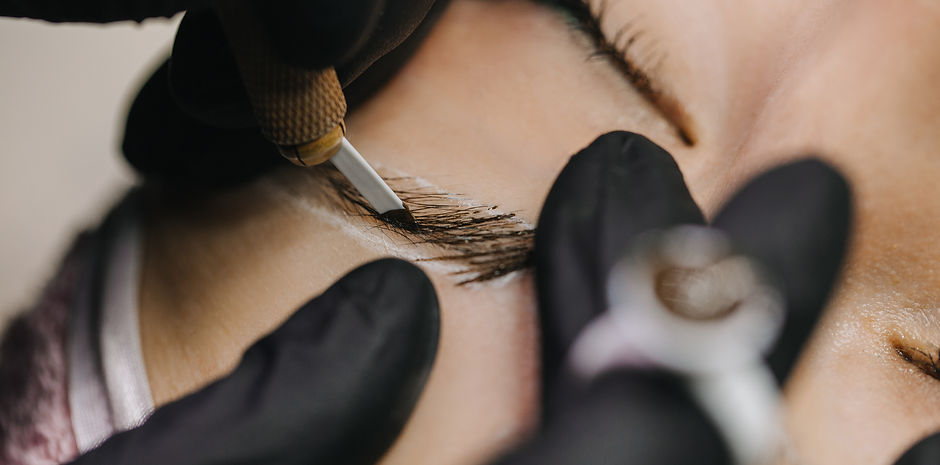 Hands in black gloves hold the manipulator with the microblading needle and draw her hair