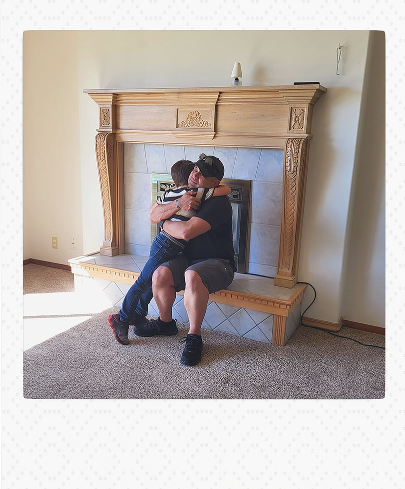 A happy client embraces a young child in front of a beautifully crafted wooden fireplace inside their new home.