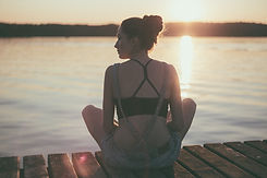 woman sitting cross legged on a wodden dock next to a lake at sunset