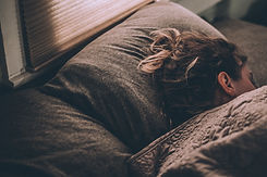 a woman sleeping in bed with gray bedding, bed next to a window with blinds closed