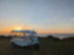 A quiet scene unfolds on the beach as the sun sets, with a white tuk-tuk parked and a single passenger sitting inside.