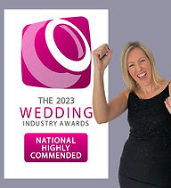 Kelly Hawes Celebrant picking up her award at The Wedding Industry Awards 2023.  Kelly is wearing a black sparkly dress and standing in front of the banner National Highly Commended.