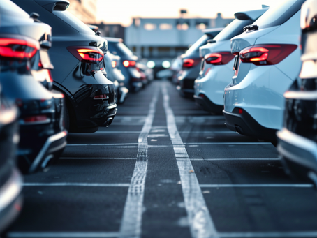 Mehrere moderne Autos stehen dicht an dicht in Reihen auf einem Parkplatz; die Rücklichter leuchten und erzeugen eine abendliche Stimmung.