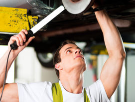 Ein KFZ-Mechaniker prüft einen Gebrauchtwagen auf einer Hebebühne