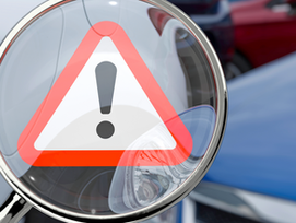 Eine Lupe vergrößert ein dreieckiges Warnsymbol mit Ausrufezeichen, das vor möglichen Risiken beim Autokauf warnen soll; im Hintergrund stehen Autos.