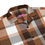 Thumbnail: A close-up view of a brown plaid unisex button-up shirt