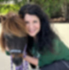 Woman smiling while hugging a miniature horse wearing a halter.