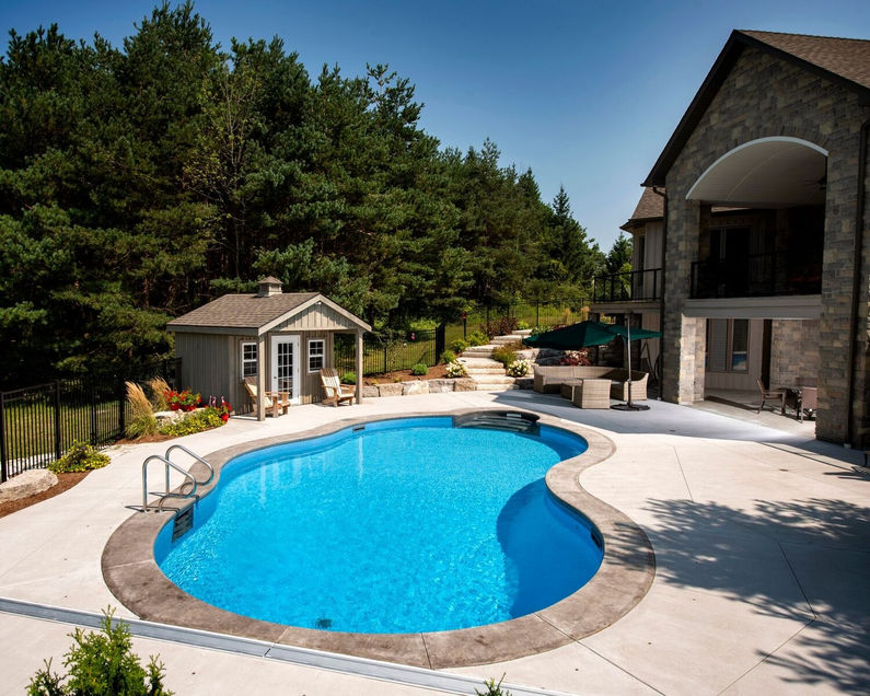 kidney shape swimming pool, forst, evergreen trees, steel-wall lined pool, large home, stone brick house, hardscape, landscape, fenced yard.