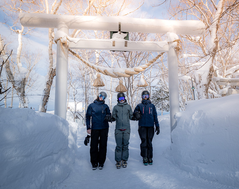 Three skiers standing underneath a torii gate in the snow at Otaru Tenguyama ski resort, Hokkaido, Japan.