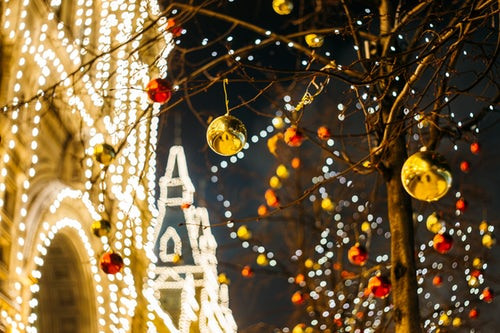 Christmas lights and decorations hanging from a tree outside a brightly lit building at night