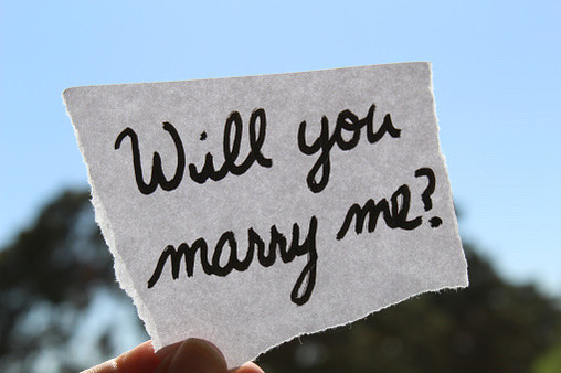 A piece of white paper with the words Will You Marry Me handwritten in black ink