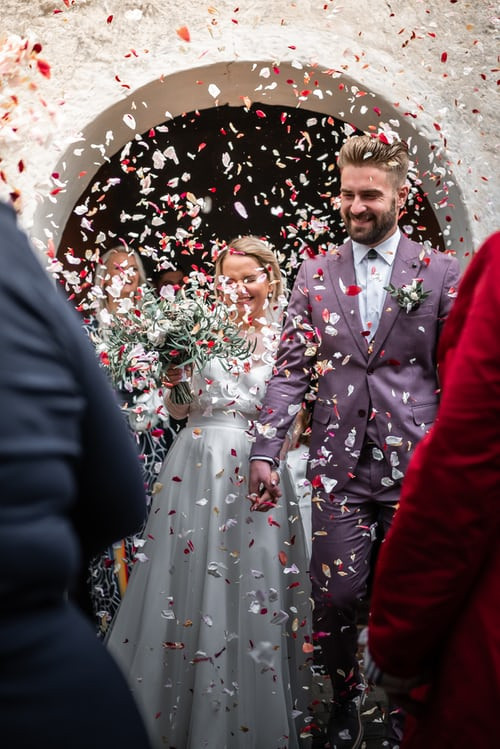 Modern bride and groom covered in confetti. Groom wears lilac coloured suit
