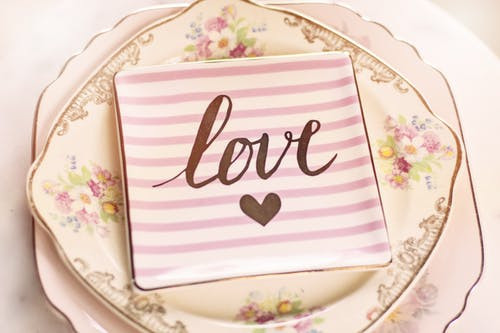 The word love printed on a square china plate sitting on floral vintage china plates