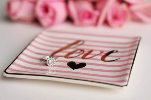 Pink and white striped trinket dish with the word Love in gold letters and and a diamond engagement ring