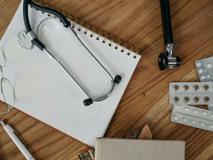 Ein Tisch, auf dem ein Stethoskop, Medikamente und ein Schreibblock liegen.