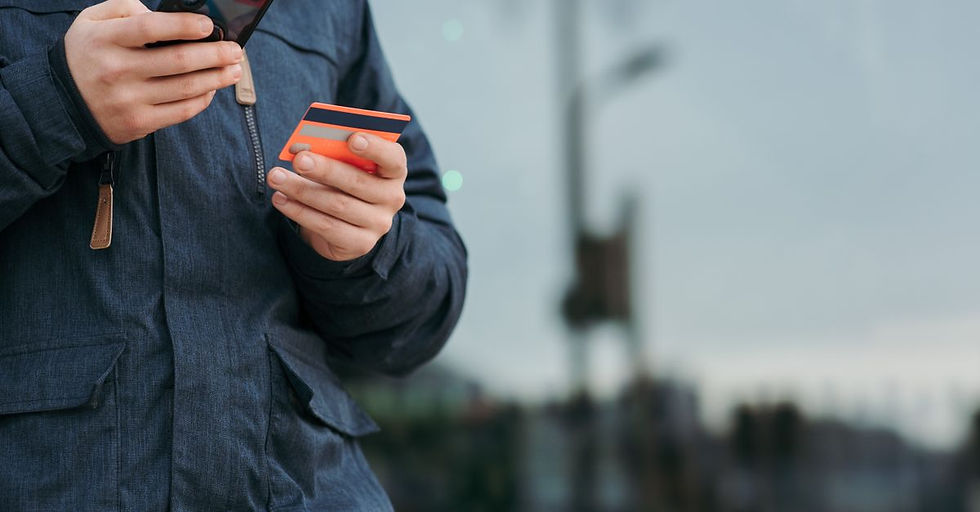 Crop anonymous man in warm clothes holding credit card and browsing smartphone while standing on street in daytime