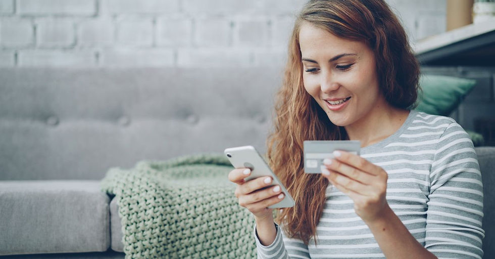 A smiling woman uses her smartphone and credit card for online shopping in a cozy living room.