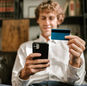 A man smiles while using his smartphone and credit card for online shopping.