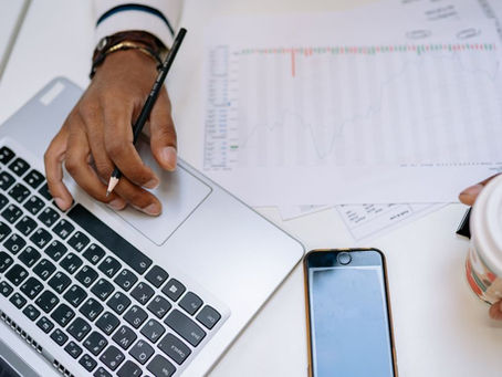 A businessman holding coffee and using a laptop at a desk with charts and a smartphone.