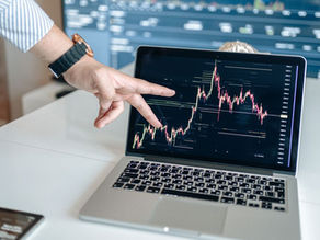 A person pointing at a laptop displaying a cryptocurrency market chart, indicating data analysis.