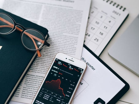 A stylish workspace featuring financial documents, eyeglasses, an iPhone displaying stock data, and a laptop.