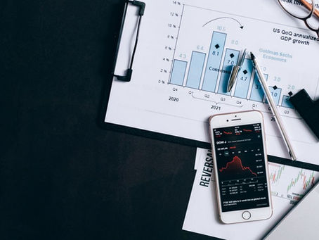 Top view of financial reports, smartphone showing stock market data, and a laptop on desk.