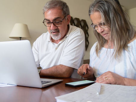 Senior couple working together on documents with laptop and phone at home.