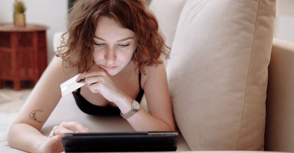 Young woman using a tablet and credit card for online shopping, lying on a couch indoors.