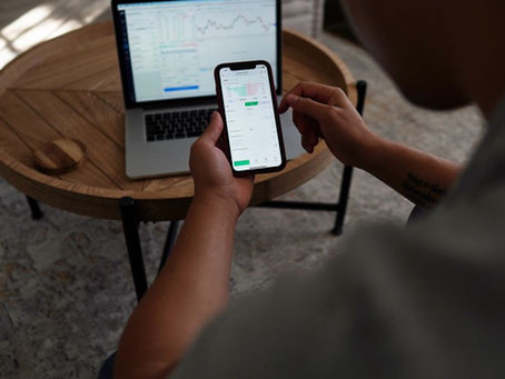 Man trading stocks online using smartphone and laptop. Indoor setting, focus on technology and finance.