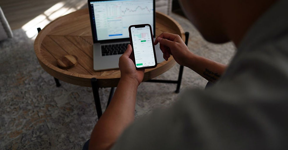 Man trading stocks online using smartphone and laptop. Indoor setting, focus on technology and finance.