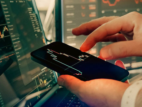 Hands interact with smartphone for analyzing cryptocurrency trading on digital screens.