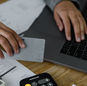 Close-up of a person using a credit card and laptop in a financial setting with cash and calculator.
